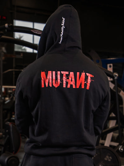 Back view of an athlete posing in the gym, wearing the Black Mutant Patched Zip-Up Gym Hoodie. The hoodie features a Red Mutant logo on the back and the white Mutant motto 'Leave Humanity Behind' on the hood.