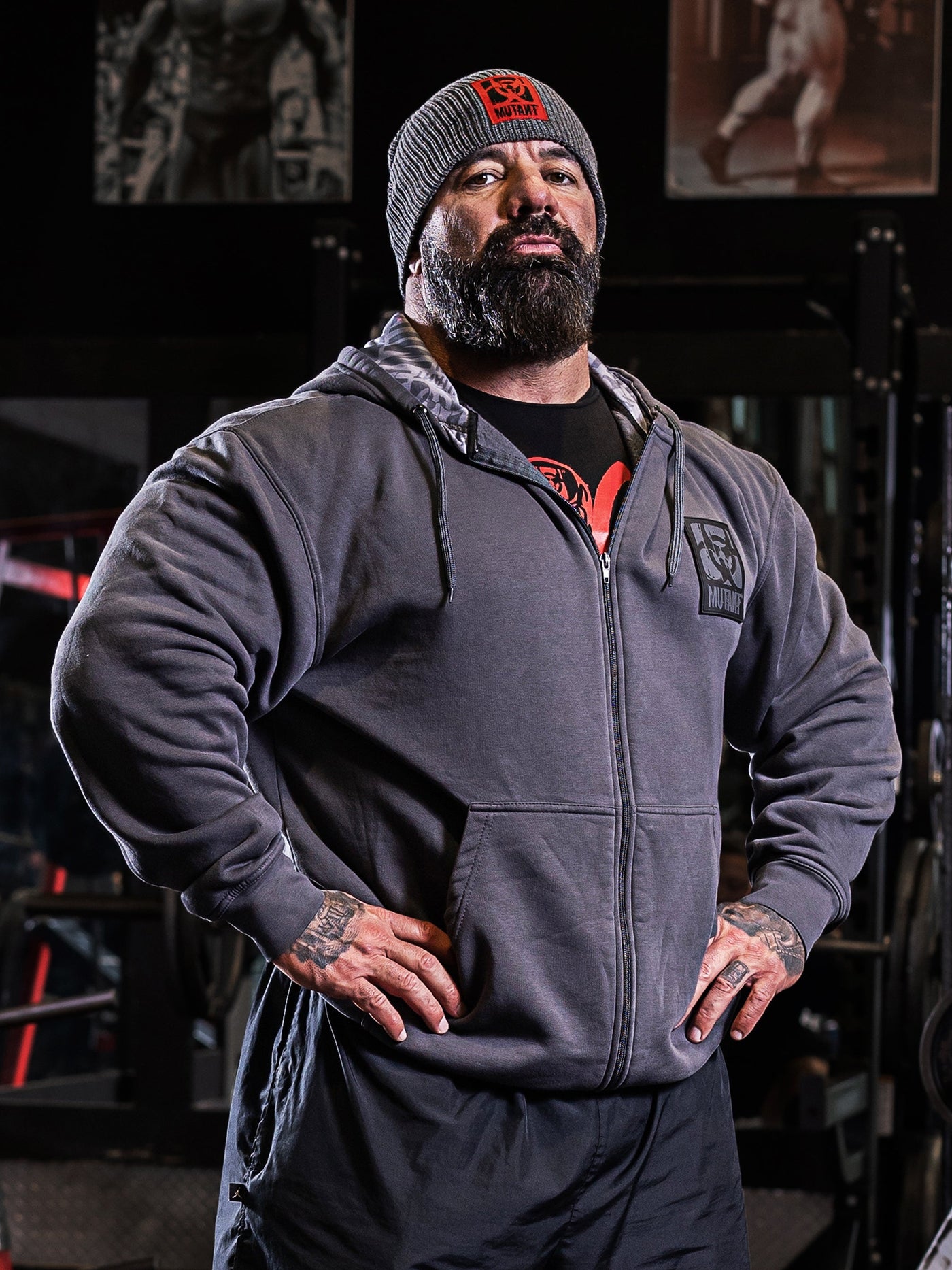 Dusty Hanshaw posing in the gym wearing Grey Mutant Patched Zip-Up Gym Hoodie with black Mutant logo patch on left chest. Two pockets and light grey hood lining with watermarked Mutant logo.