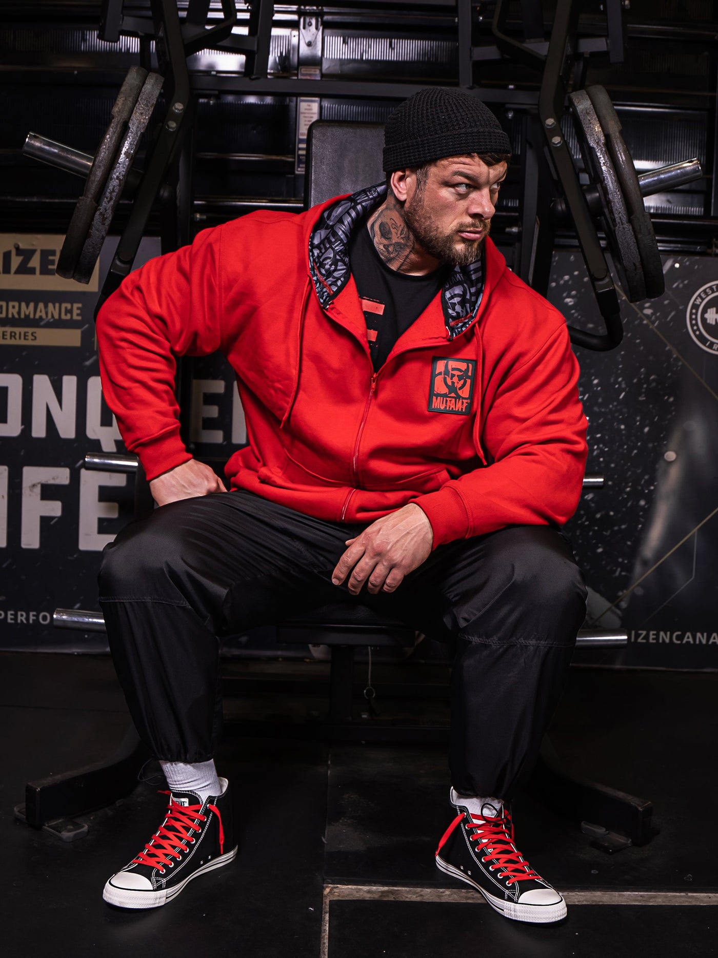 Mutant athlete Jamie Christian posing in the gym wearing Red Mutant Patched Zip-Up Gym Hoodie with a black and red Mutant logo patch on left chest. Two pockets and grey hood lining with watermarked Mutant logo.